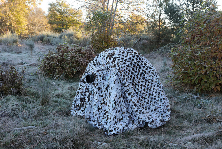 pixelpenguin- Een persoon zit midden in een veld bedekt met camouflagenetten.
