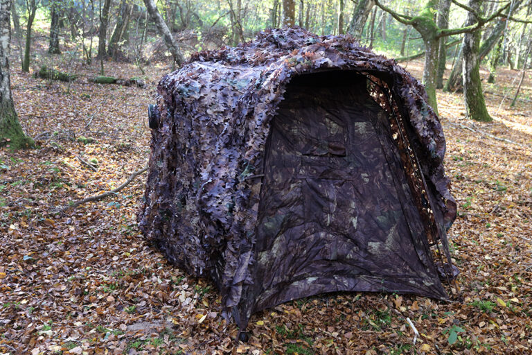 pixelpenguin- Een camouflagenet genesteld tussen de bomen in het bos.