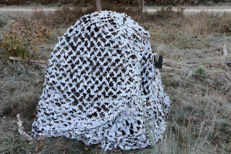 pixelpenguin- Een camouflagenet dat een boom in een veld bedekt.