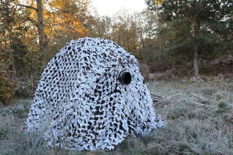 pixelpenguin- Een camouflagenetafdekking in het bos.