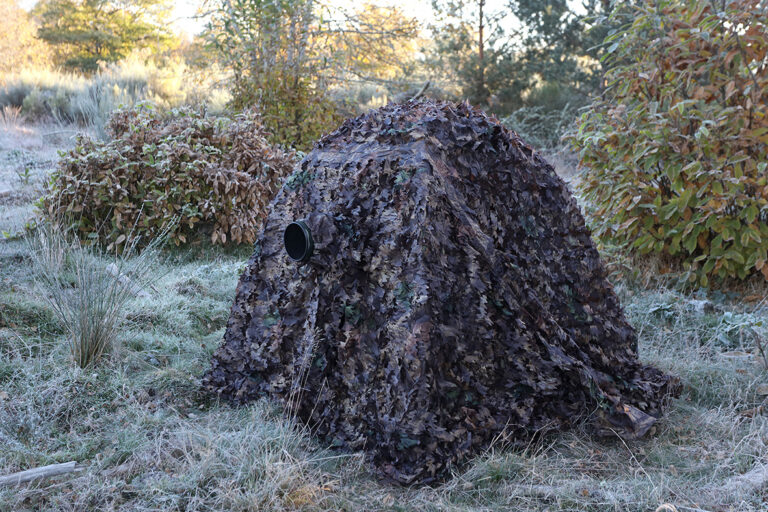 pixelpenguin- Een camouflagenettent midden in een veld.